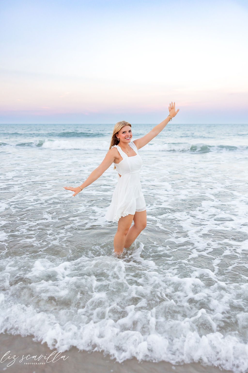 Ryann smiling with her arms out as waves wash around her feet 