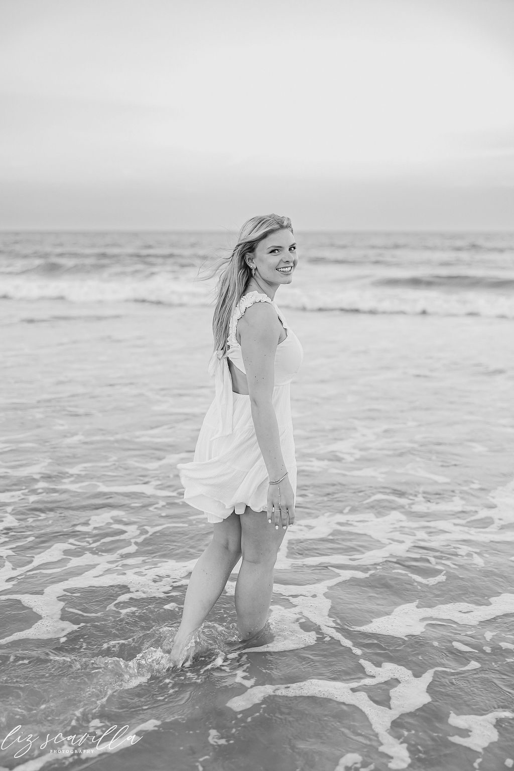 Black-and-white senior portrait of Ryann looking back beside the ocean